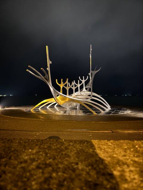 Sculpture resembling a boat structure at night.