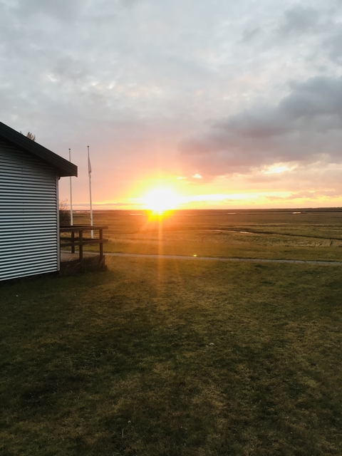 A sunset view over a flat landscape with a small building.
