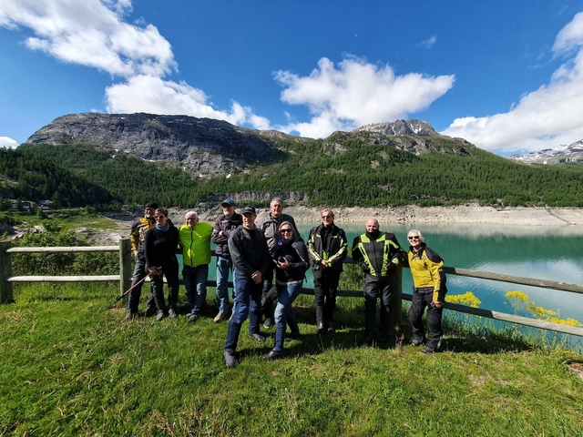 A group of motorcyclists standing by a scenic lake and mountains.