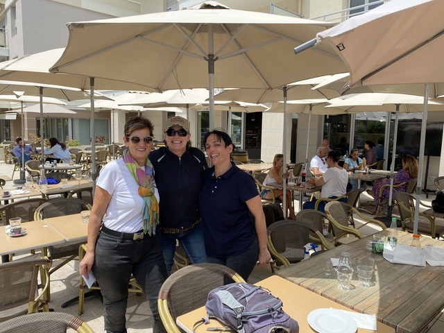 Three women posing at an outdoor cafe with umbrellas.