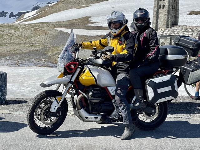 Two people on a motorcycle near a snowy mountain landscape.