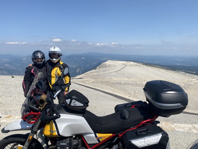Two people on a motorcycle at a mountaintop viewpoint.