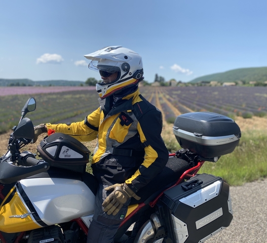 A motorcyclist in a lavender field with a village in the distance.