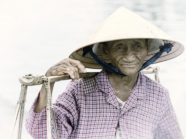 Elderly person wearing a traditional hat, carrying items.