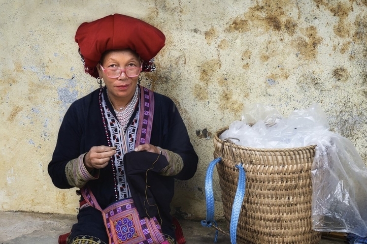 Person in traditional attire sitting with a basket, sewing.