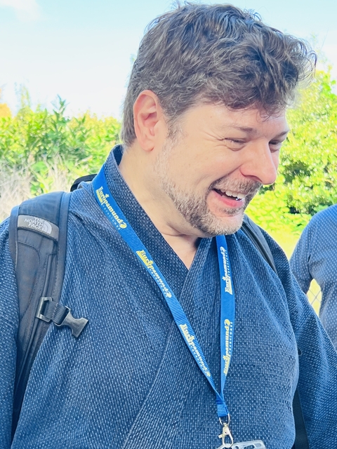       Person wearing a tour badge, smiling outdoors.
  