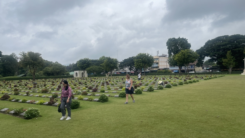 People strolling in a well-maintained cemetery with trees in the background.