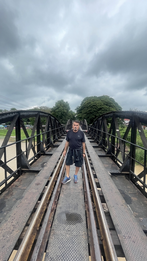 Man on a bridge with large black railings, trees in the background.