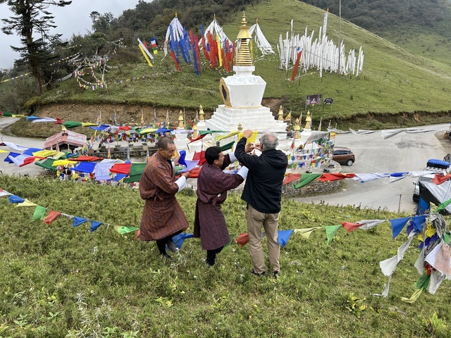 Three men hanging prayer flags near a white stupa.