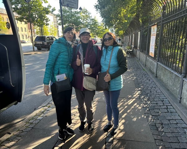 Three people standing on a cobblestone street, smiling at the camera.
