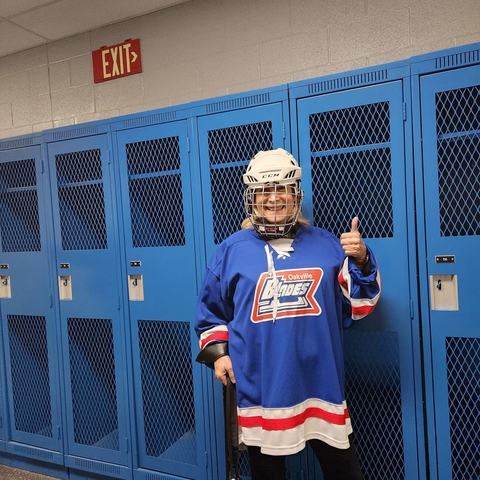 Person posing in a hockey uniform in a locker room.