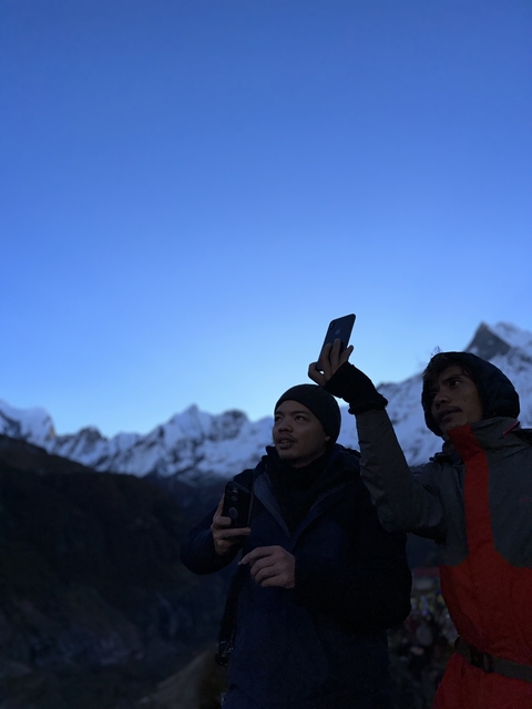       Two people taking a photo with snow-capped peaks in the background.
  