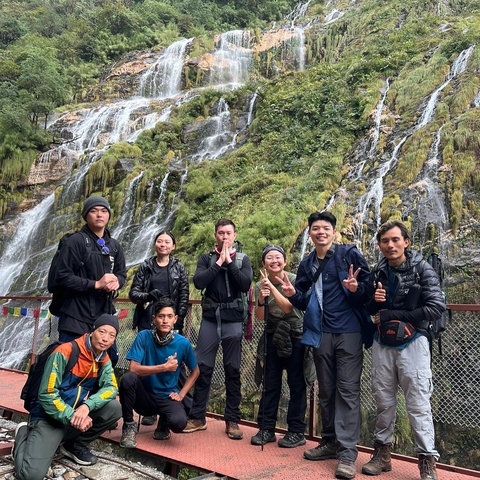       Group of people posing in front of a scenic waterfall in a natural setting.
  