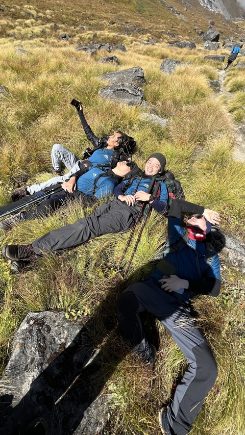       Hikers resting on grass with trekking poles.
  