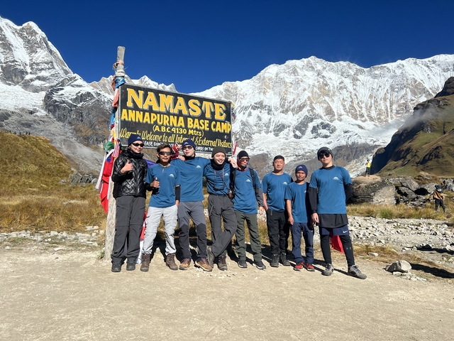       Group of hikers at Annapurna Base Camp with a welcome sign.
  