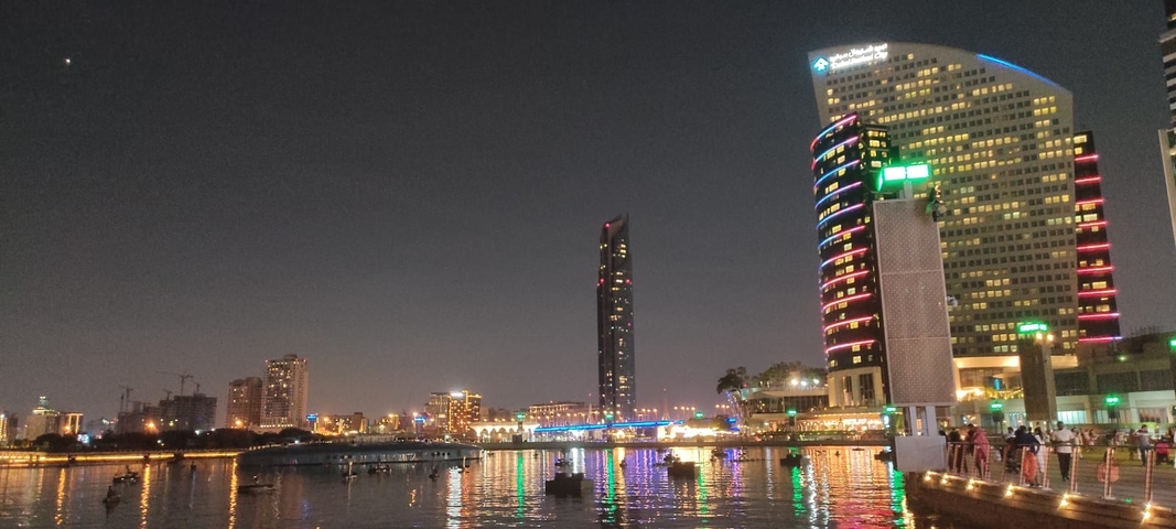 City skyline with colorful lights reflecting on water at night.