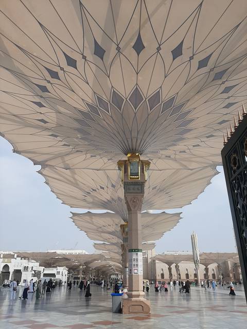 Large architectural umbrella structures in a public square, with people walking around.