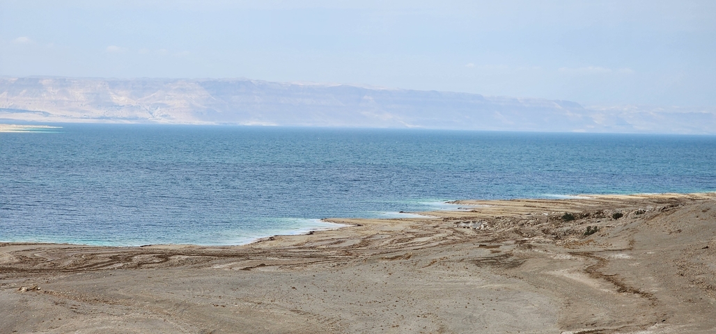A view of a coastal area with clear blue water and distant mountains.