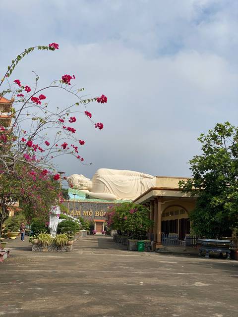 Reclining Buddha statue in a garden with flowering plants.
