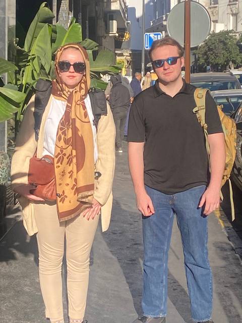       Two people standing outdoors, one in a headscarf.
  