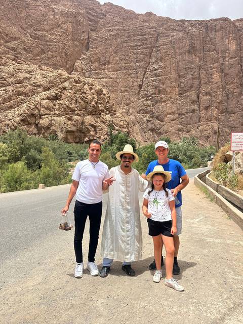       Group of people posing on a road with rocky cliffs in the background.
  