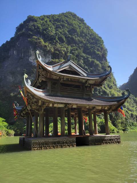 Traditional pagoda on a river with a limestone cliff backdrop.