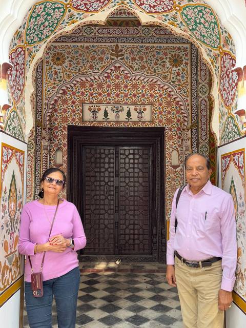       Couple standing in front of ornate architecture with decorative tiles.
  