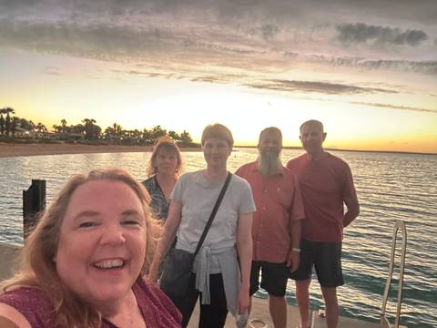 Smiling group taking a selfie with a sunset over water.