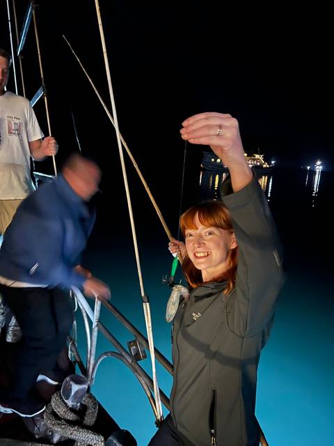       People fishing off the side of a boat at night.
  
