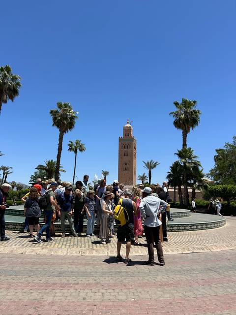Tourists gathered near a historic mosque with palm trees.