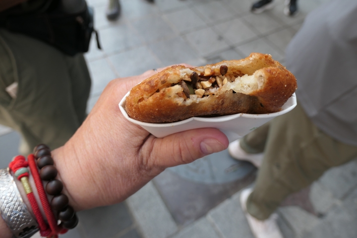 Close-up of a hand holding a piece of street food with filling.