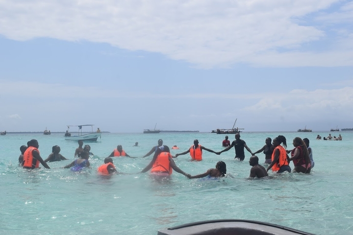 Group of people holding hands in the water wearing life vests.
