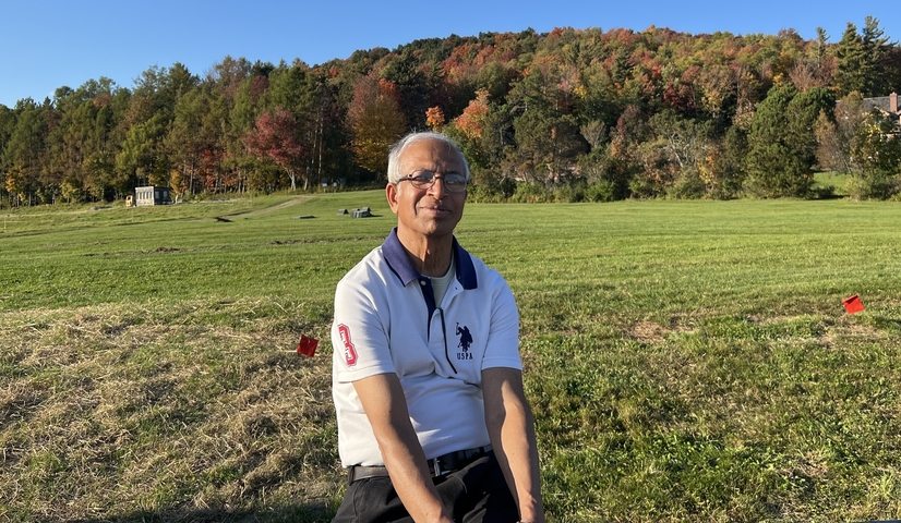 Man sitting on a grassy field with autumn foliage.