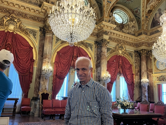       Man inside a luxurious room with chandeliers and red curtains.
  
