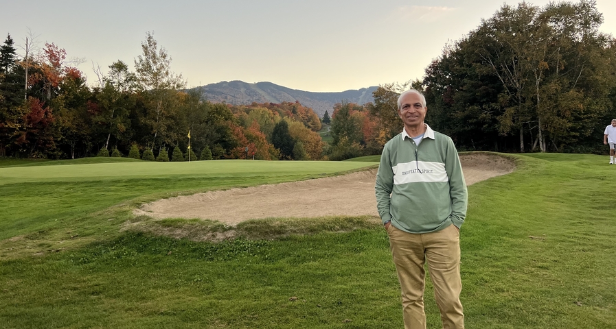       Man posing on a golf course with mountains in the background.
  