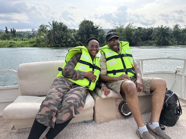       Two people wearing life vests sitting on a boat with greenery in the background.
  