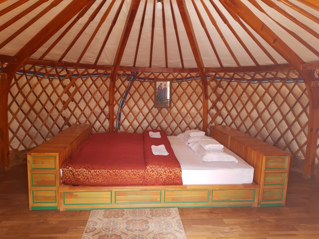       Interior of a traditional Mongolian ger with a bed and wooden decor.
  