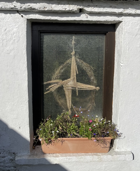 Wicker cross displayed on a wall with flowers.