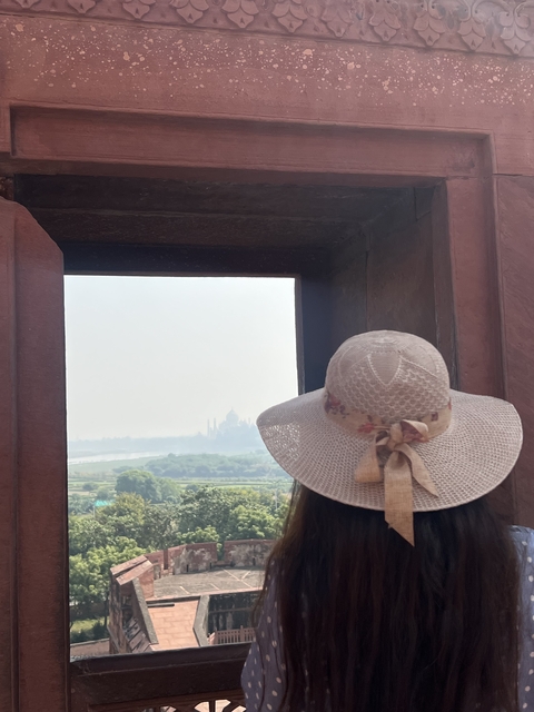       Person with a hat looking through a window towards the Taj Mahal.
  