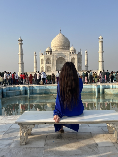       Person in blue stands near a fountain with the Taj Mahal in the background.
  