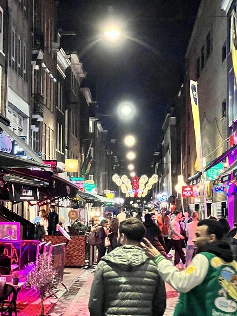       A street at night with colorful lights and people walking around.
  