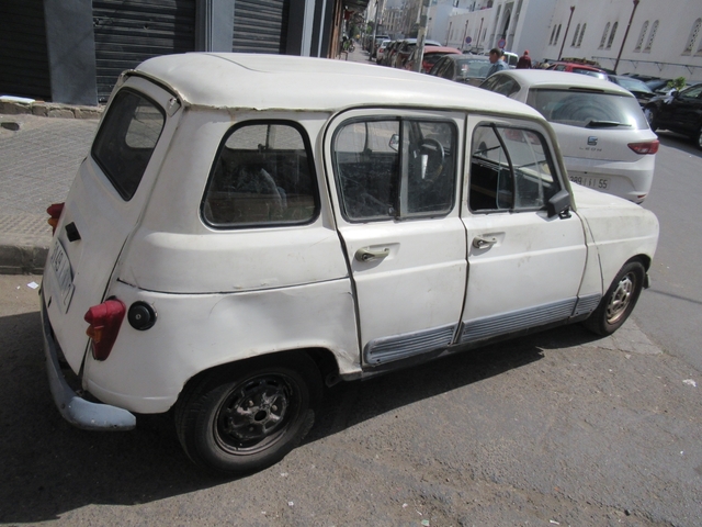       An older white car parked on a street.
  