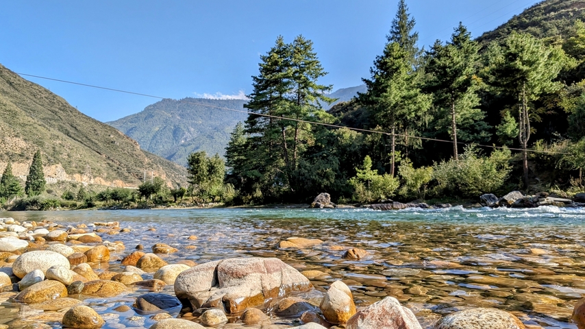       Rocky riverbank with mountains in the background in Bhutan.
  
