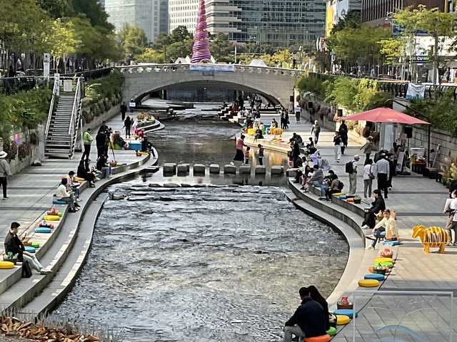       Urban stream with people seated along its banks.
  