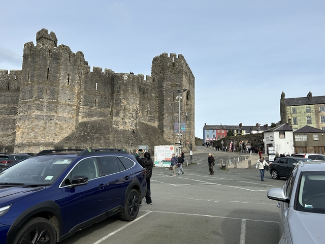 Castle with vehicles and people in front.