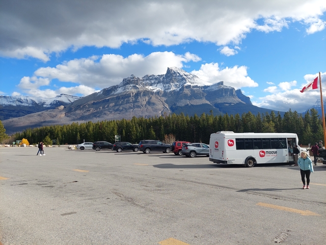 Parking lot with a tour bus, cars, and a snowy mountain in the background.