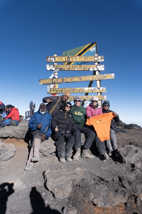       People celebrating with a sign at the summit of Uhuru Peak, Tanzania.
  