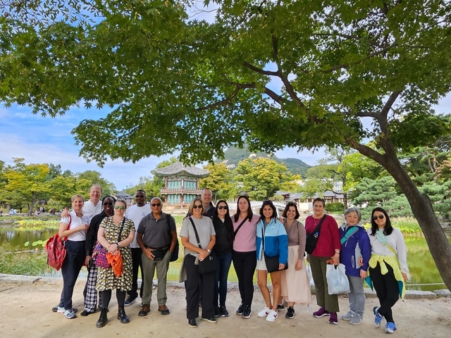 Tourists posing in front of a pond with a traditional Korean building in the background.