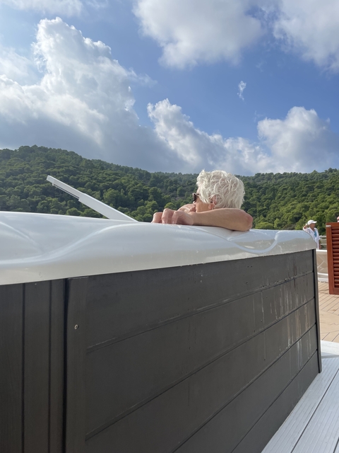 Person relaxing on a yacht with green hills in the background.