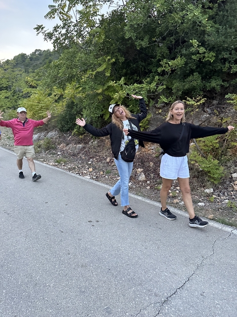       Two women and a man walking happily on a road surrounded by foliage.
  